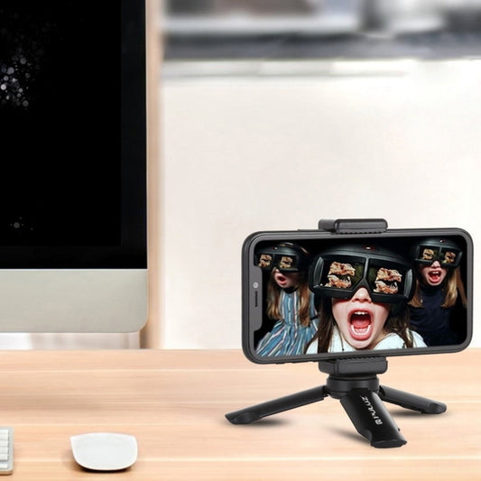 Smartphone with a small tripod on a desk next to a computer monitor