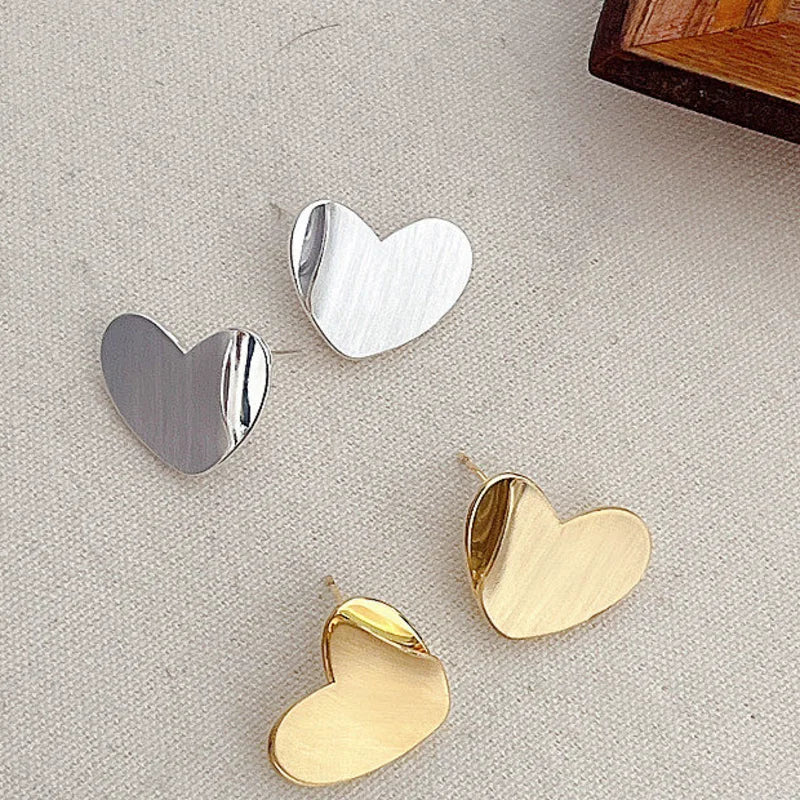 Brushed heart stud earrings in gold and silver on linen