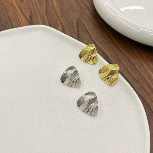 Brushed triangle stud earrings in gold and silver on a white plate