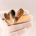 Large polished gold heart stud earrings held on a white glove
