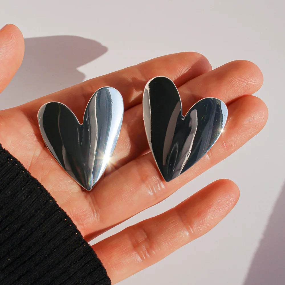 Silver heart stud earrings in the palm of a hand to show their size