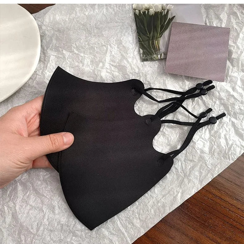 Hand holding two black face masks showing the adjustable ear loop sliders