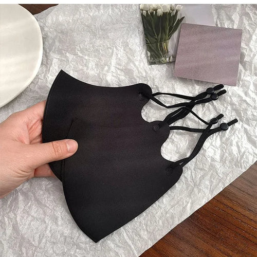 Hand holding two black face masks showing the adjustable ear loop sliders
