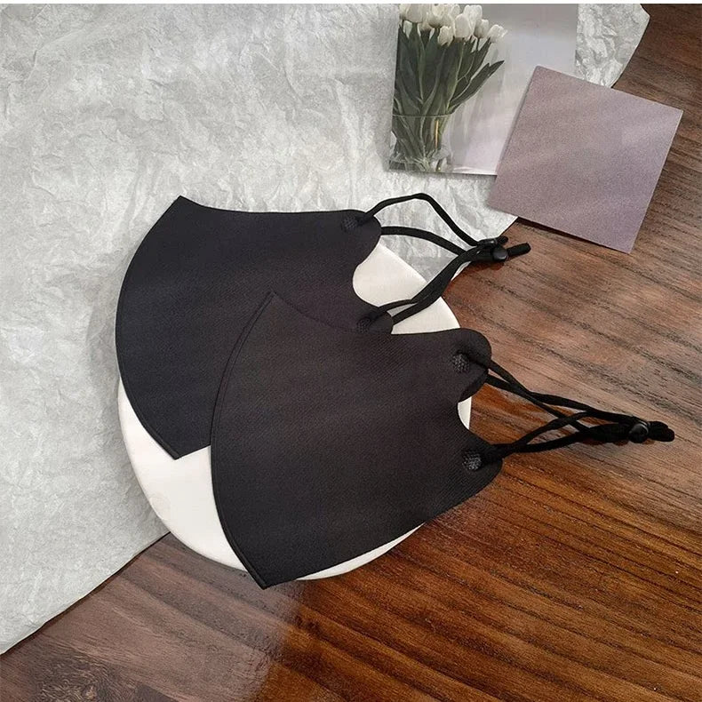Two black ice silk 3D face masks with adjustable ear loops on a white plate