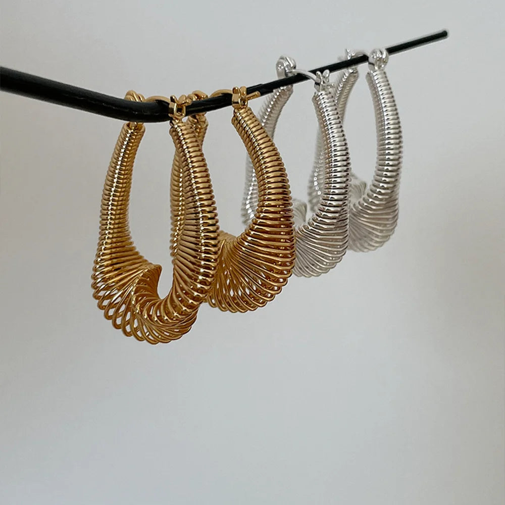 Gold and silver spiral coil hoop earrings hanging side by side, showing their shape