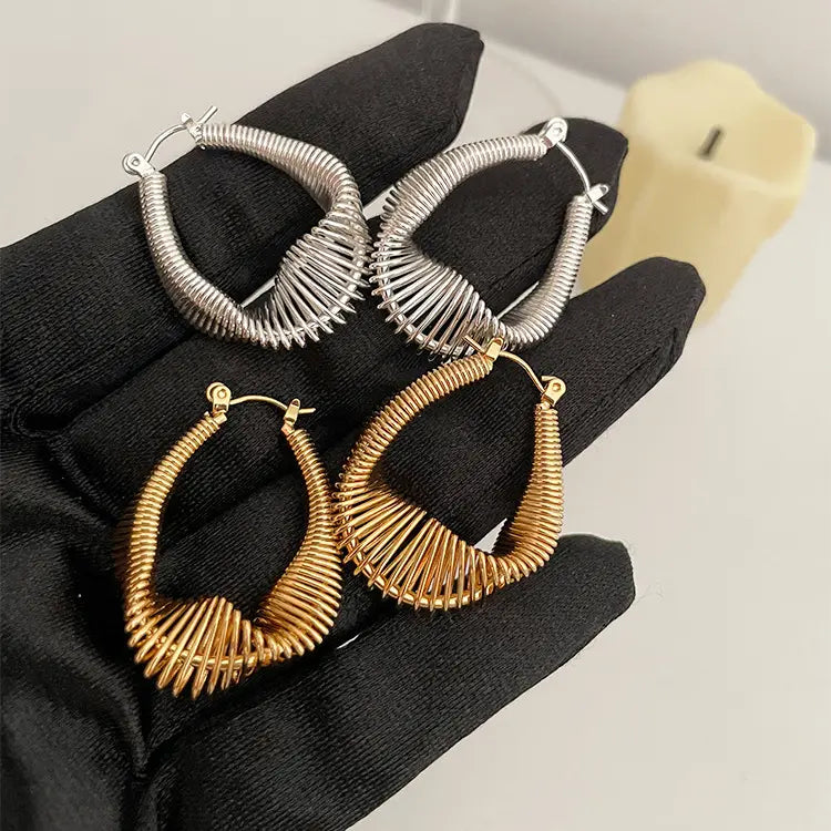 Gold and silver spiral coil hoop earrings held on a black gloved hand