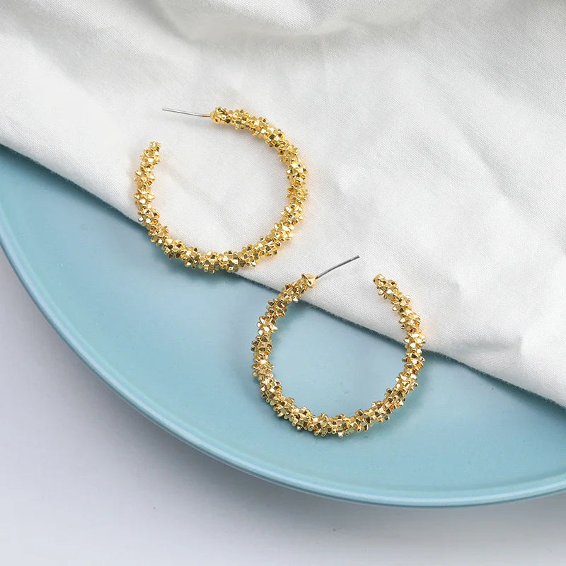 Gold textured cluster C-hoop earrings on a blue plate with white linen