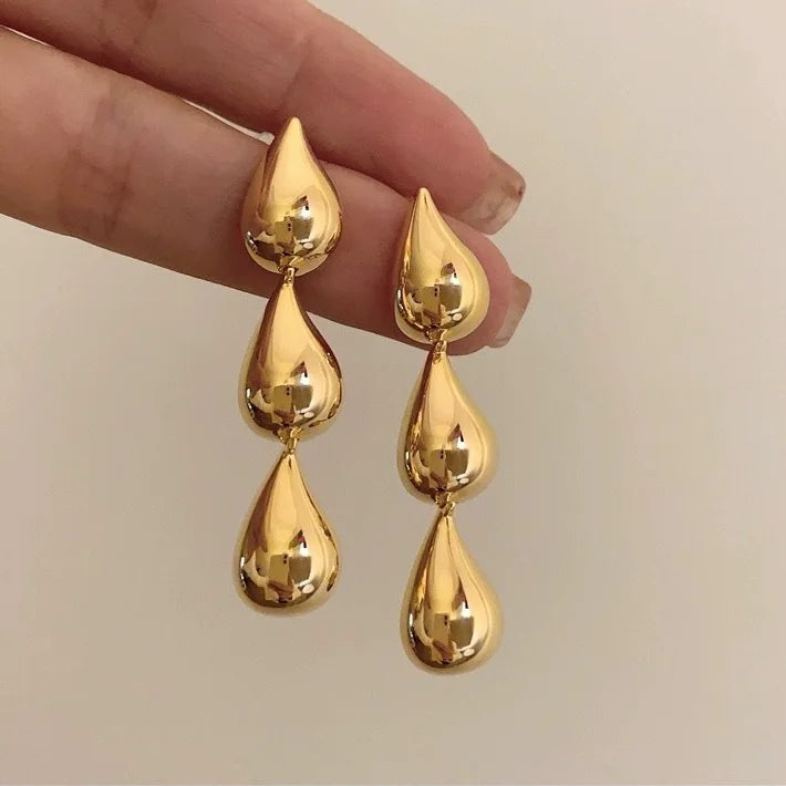 Gold triple teardrop drop earrings held between fingers to show their length
