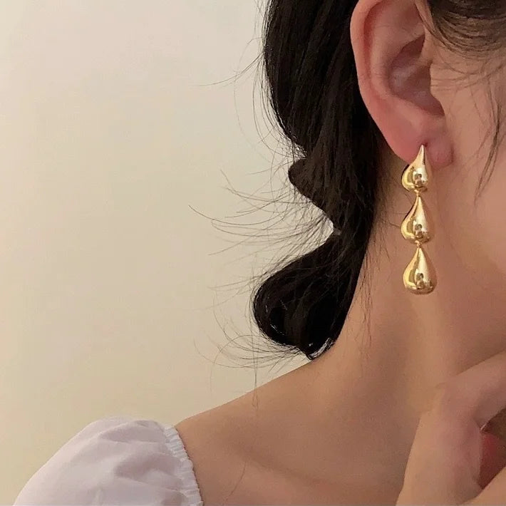 Gold triple teardrop drop earring worn on the ear