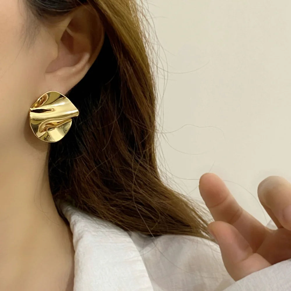 Gold wavy disc stud earring worn on the ear