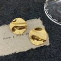 Pair of gold wavy disc stud earrings with a mirror finish on textured paper