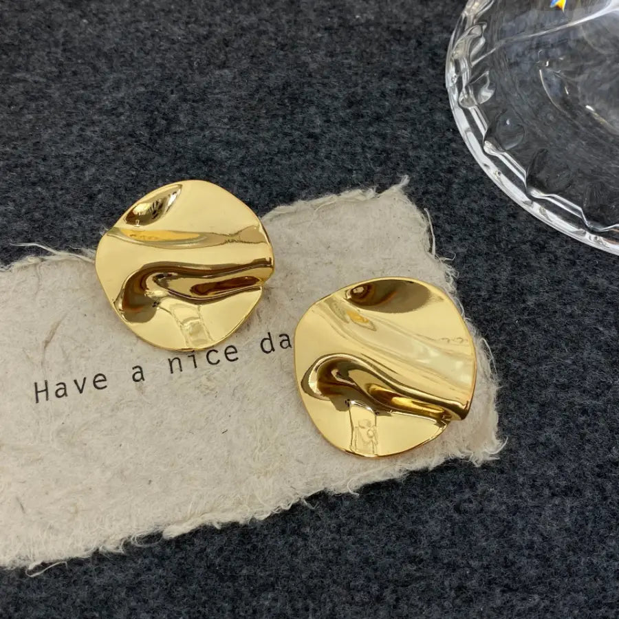 Pair of gold wavy disc stud earrings with a mirror finish on textured paper