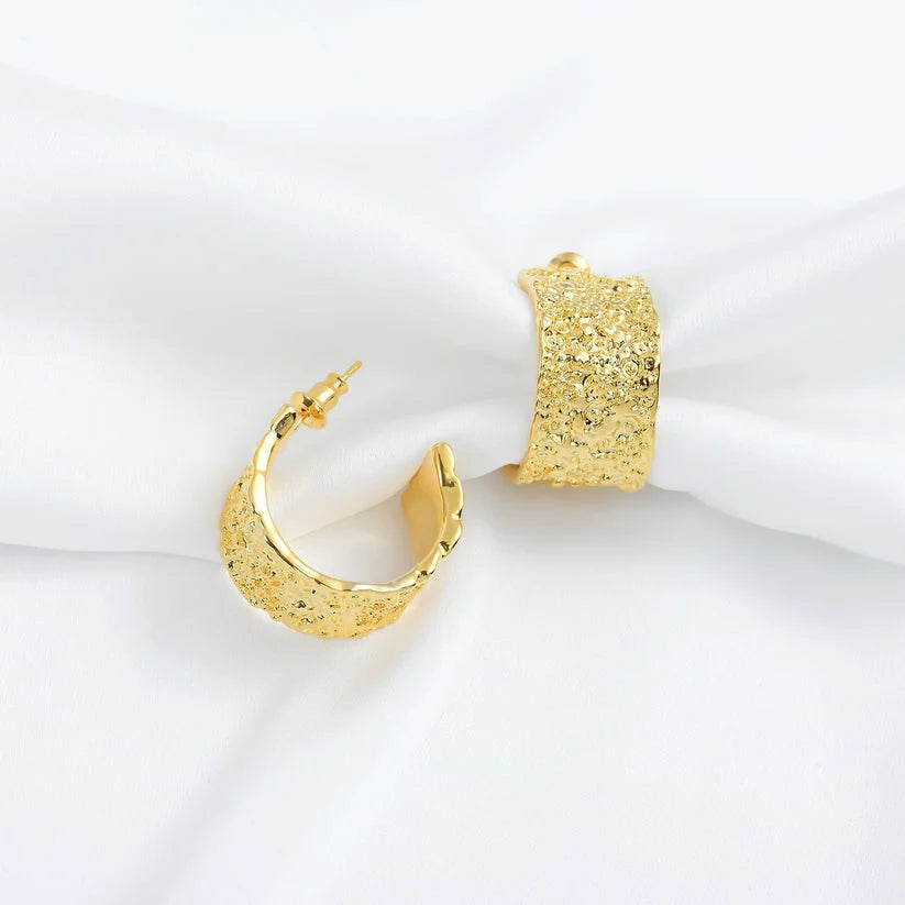 Wide gold textured C-hoop earrings on white satin
